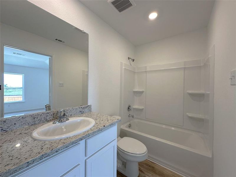 Primary bathroom includes granite counters, designer white cabinetry and luxury vinyl plank flooring.