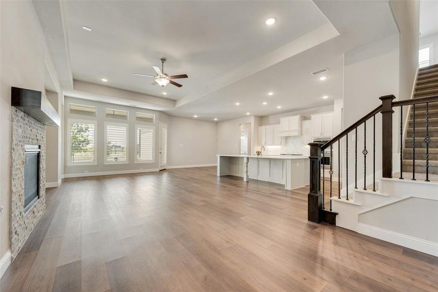 Unfurnished living room with ceiling fan, light wood-type flooring, and a tray ceiling