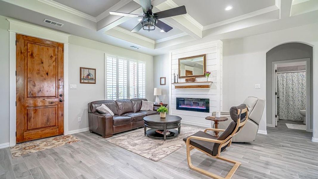 Living room featuring ceiling fan, beamed ceiling, coffered ceiling, a fireplace, and light hardwood / wood-style floors