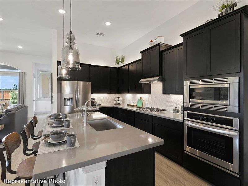 Kitchen featuring appliances with stainless steel finishes, tasteful backsplash, sink, a kitchen island with sink, and light wood-type flooring