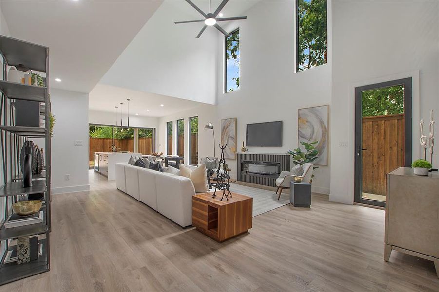 Living room with light wood-type flooring, ceiling fan with notable chandelier, and a high ceiling