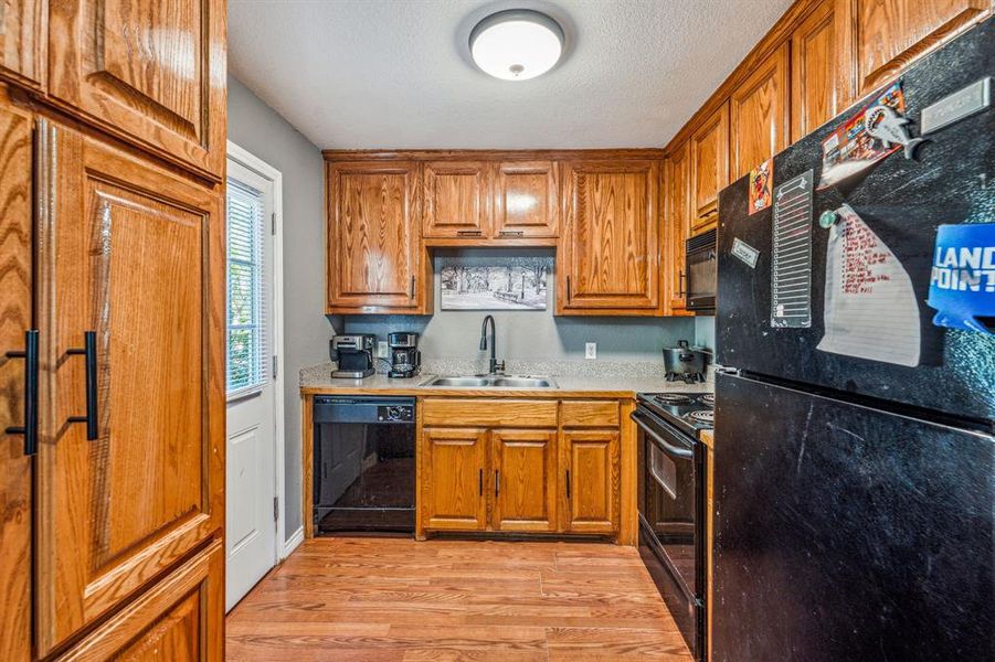 Kitchen featuring black appliances, a textured ceiling, sink, and light hardwood / wood-style flooring