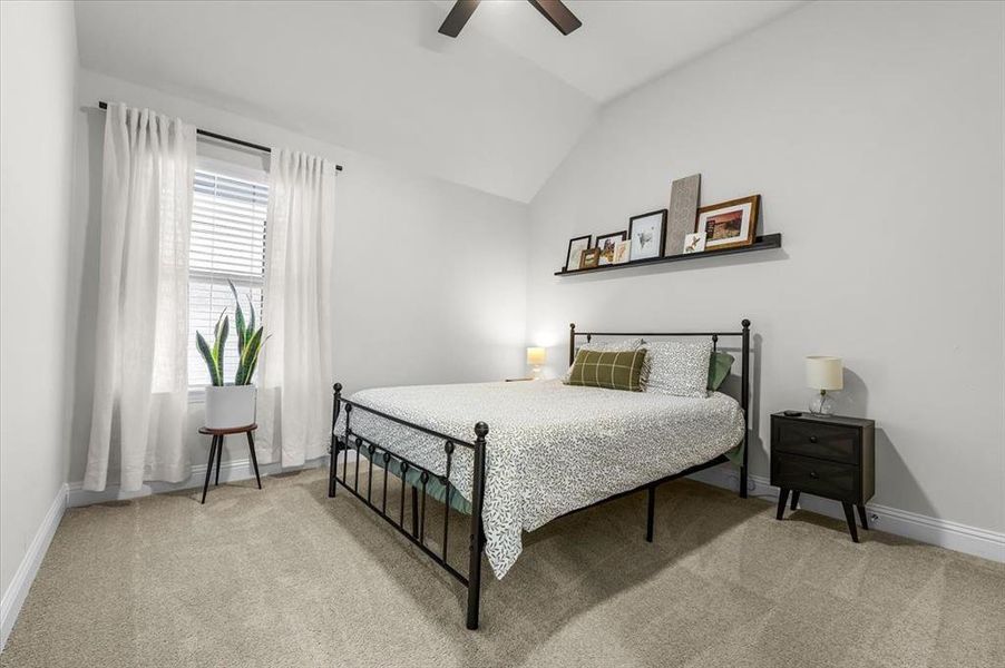 Carpeted bedroom featuring ceiling fan and vaulted ceiling