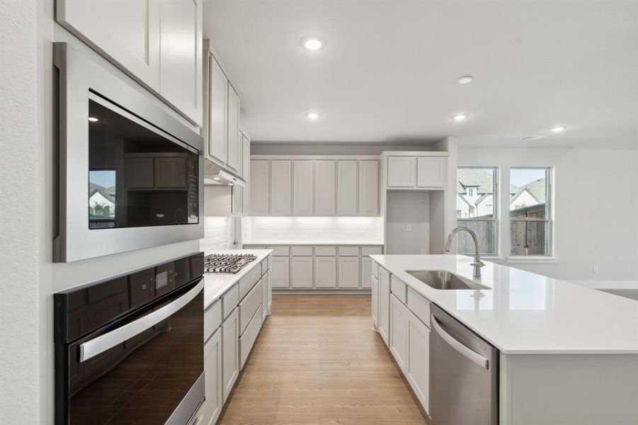 Kitchen featuring light hardwood / wood-style floors, an island with sink, stainless steel appliances, sink, and white cabinets