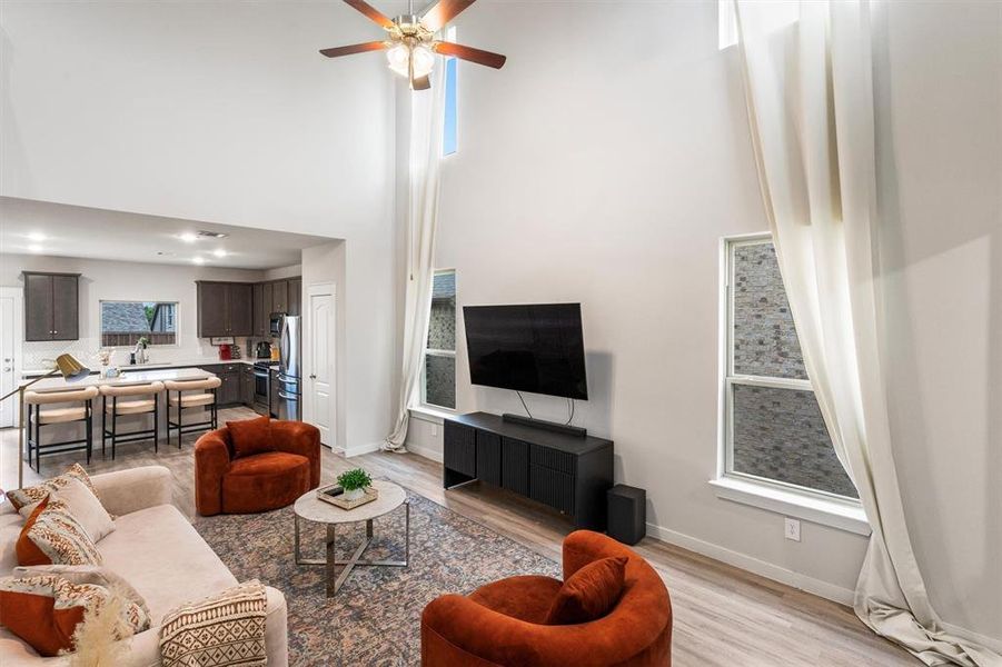 Living room with a high ceiling, light hardwood / wood-style flooring, ceiling fan, and plenty of natural light