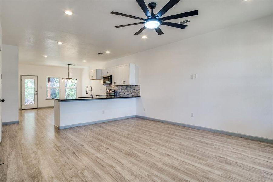 Kitchen featuring light hardwood / wood-style floors, white cabinetry, kitchen peninsula, appliances with stainless steel finishes, and decorative light fixtures