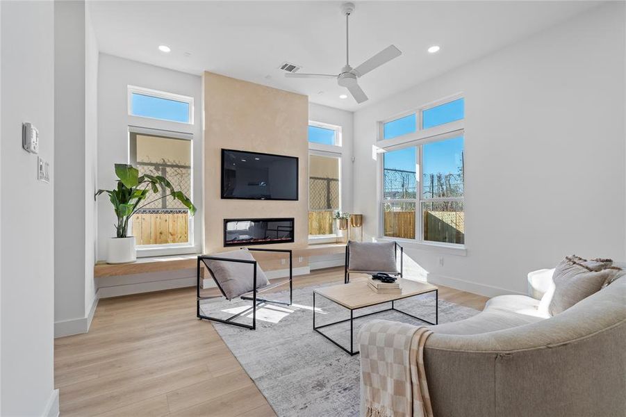 This living area exudes warmth and contemporary flair with its high ceilings, large windows, and a beautifully framed fireplace. The natural light creates an airy ambiance, perfectly complemented by the minimalistic design elements that make this space both stylish and welcoming. Ideal for relaxing or entertaining, this room is a central gathering point with undeniable appeal.