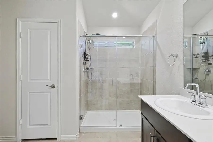 Bathroom with a shower with shower door, vanity with extensive cabinet space, and tile floors