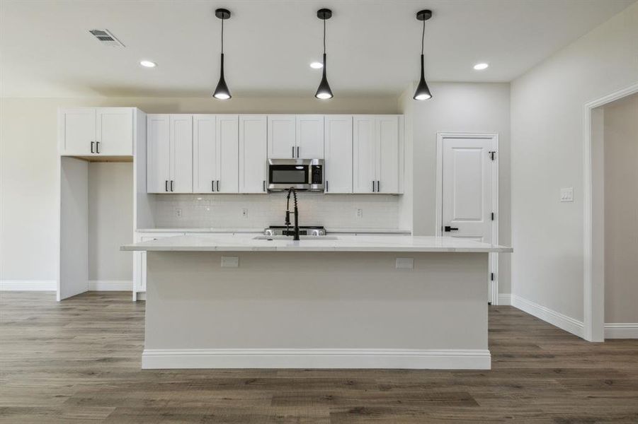 Kitchen featuring an island with sink, white cabinetry, and pendant lighting