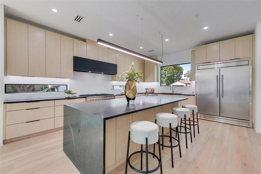 Kitchen featuring range hood, stainless steel built in refrigerator, light hardwood / wood-style flooring, and a kitchen island