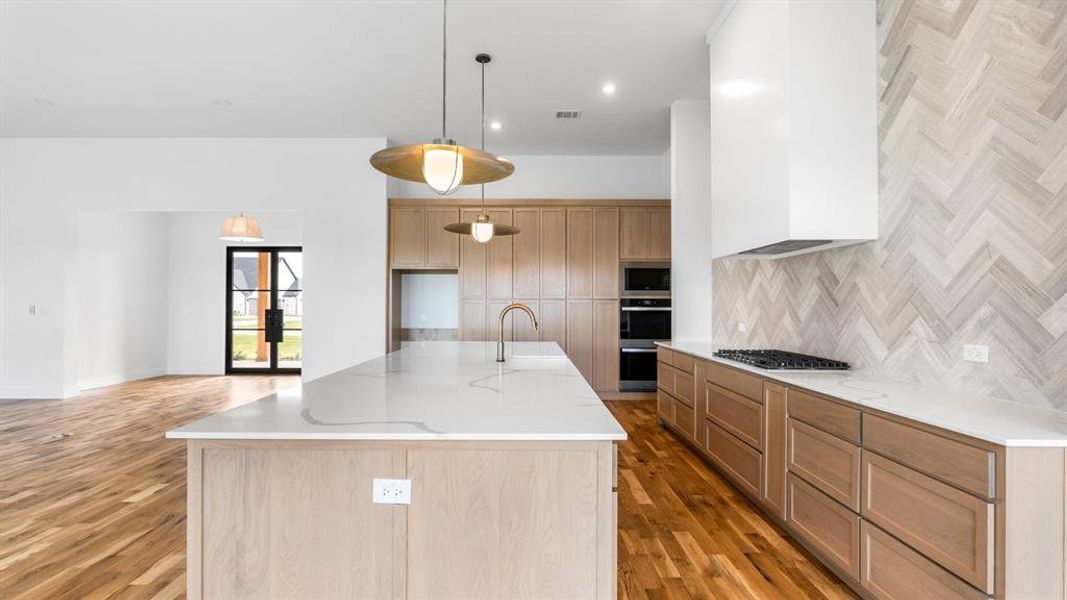 Kitchen with light stone countertops, stainless steel appliances, light hardwood / wood-style floors, and decorative light fixtures