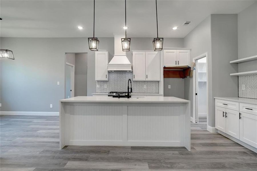 Kitchen with a kitchen island with sink, tasteful backsplash, white cabinetry, and light wood-type flooring
