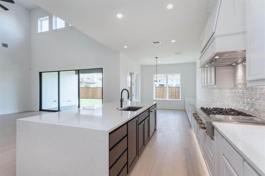 Kitchen with tasteful backsplash, sink, white cabinetry, light hardwood / wood-style floors, and pendant lighting