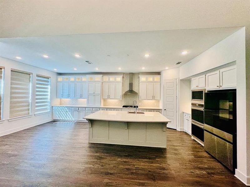 Kitchen featuring wall chimney range hood, appliances with stainless steel finishes, an island with sink, white cabinetry, and dark hardwood / wood-style floors