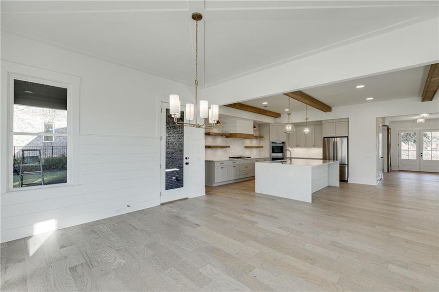 Kitchen with light wood-type flooring, a center island with sink, hanging light fixtures, and stainless steel appliances
