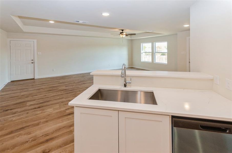 Kitchen featuring ceiling fan, sink, stainless steel dishwasher, light hardwood / wood-style flooring, and white cabinetry