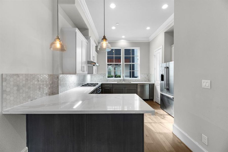 As you approach the kitchen, a spacious breakfast bar with pendant lighting provides a casual yet stylish dining spot. The gleaming quartz countertops beautifully contrast with the rich wood cabinets, creating an elegant and inviting atmosphere.