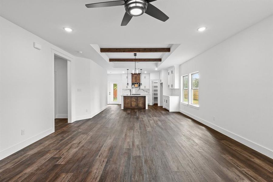 Unfurnished living room featuring ceiling fan, beam ceiling, and dark hardwood / wood-style flooring