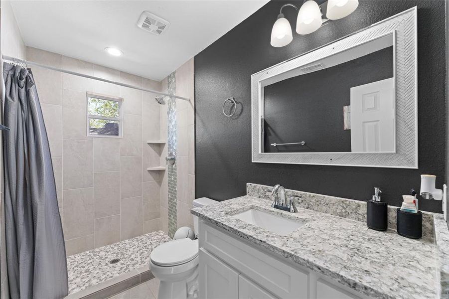 Bathroom with toilet, curtained shower, vanity, and tile patterned flooring