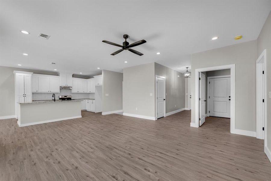 Unfurnished living room with ceiling fan with notable chandelier, light wood-type flooring, and sink