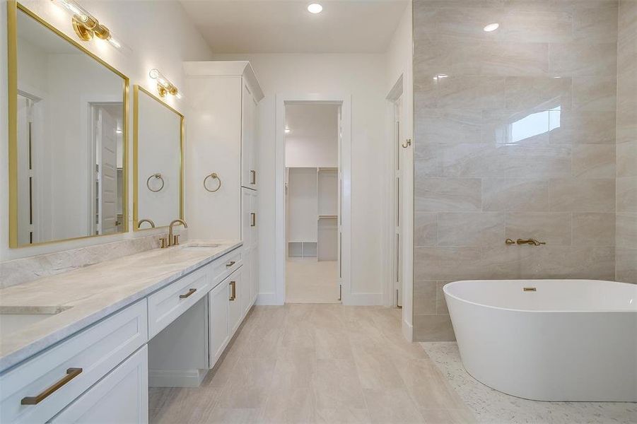 Bathroom featuring a tub, dual vanity, tile patterned floors, and tile walls