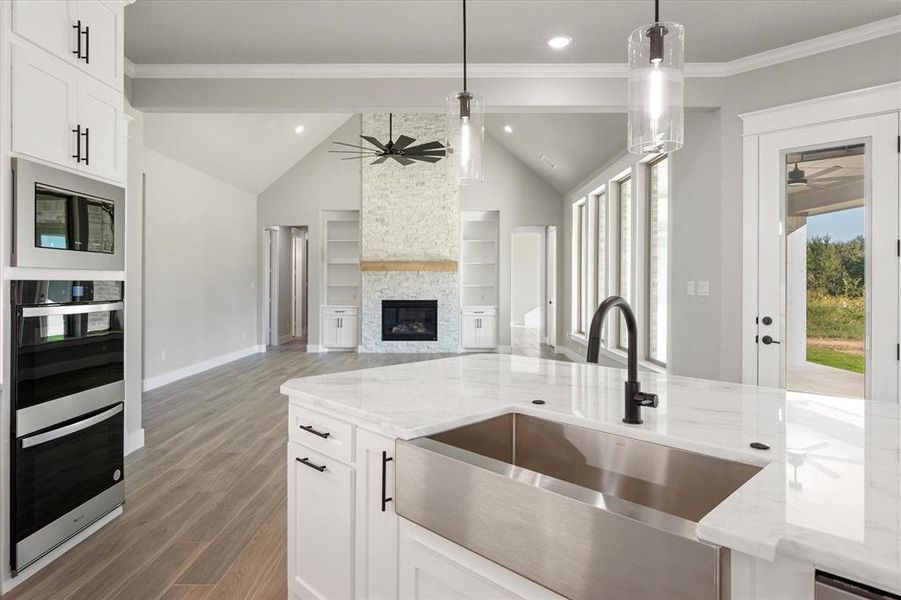 Kitchen featuring pendant lighting, sink, ceiling fan, a stone fireplace, and vaulted ceiling