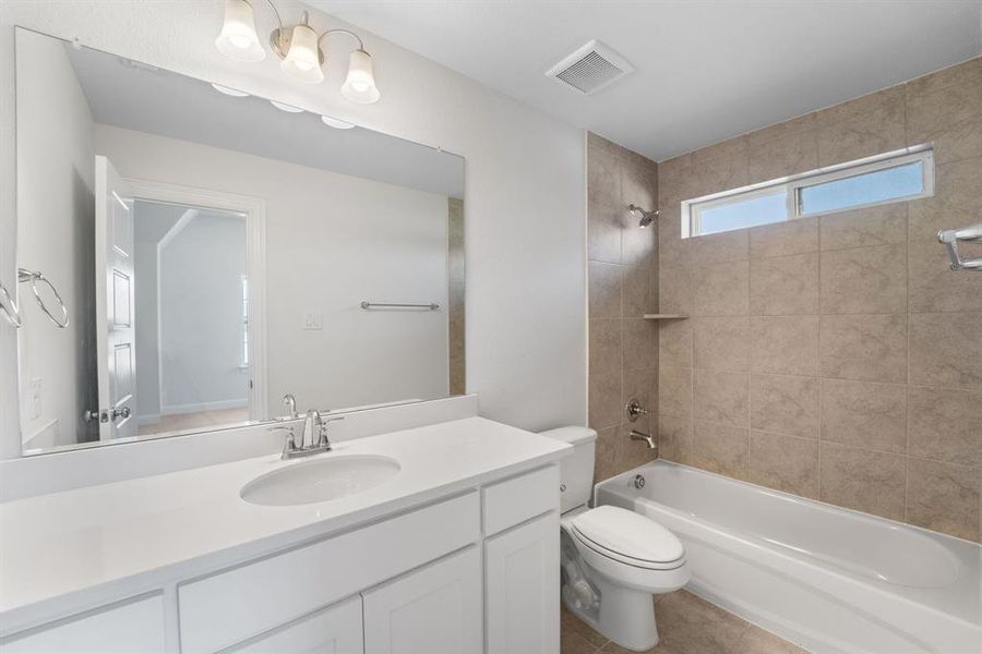 Full bathroom with tile floors, tiled shower / bath combo, vanity, and toilet