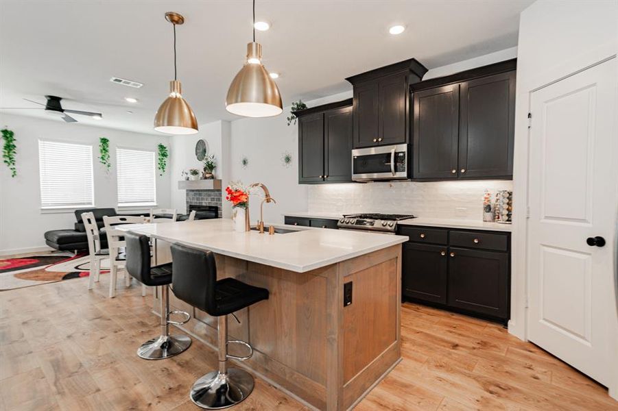Kitchen featuring appliances with stainless steel finishes, tasteful backsplash, a center island with sink, sink, and light wood-type flooring