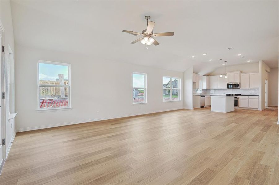 Unfurnished living room featuring a wealth of natural light, ceiling fan, light wood-type flooring, and lofted ceiling