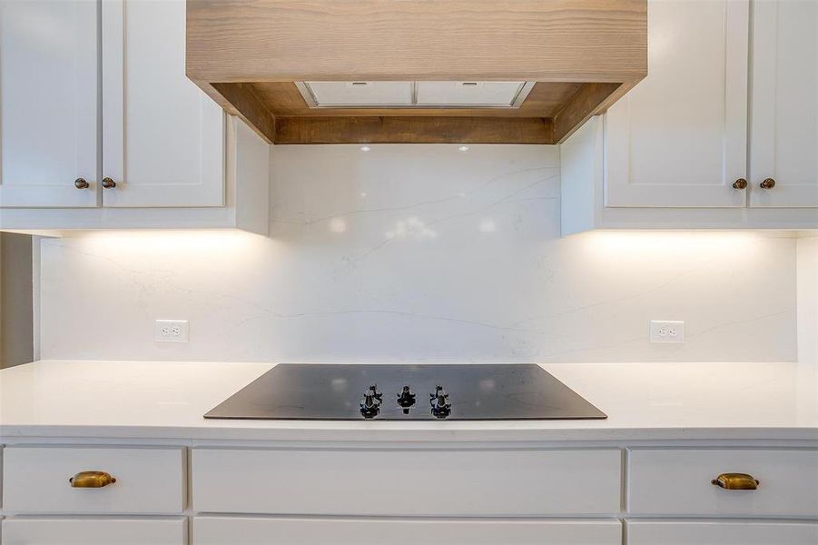 Kitchen with decorative backsplash, black electric cooktop, and white cabinets