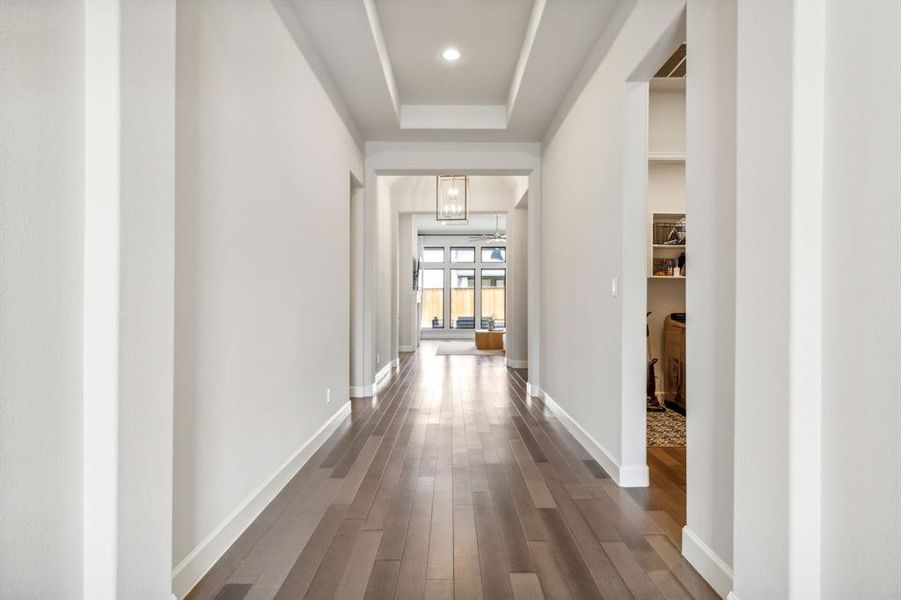 Hall with an inviting chandelier, a raised ceiling, and hardwood / wood-style floors