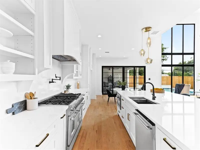 Kitchen featuring light wood-type flooring, appliances with stainless steel finishes, white cabinets, pendant lighting, and sink