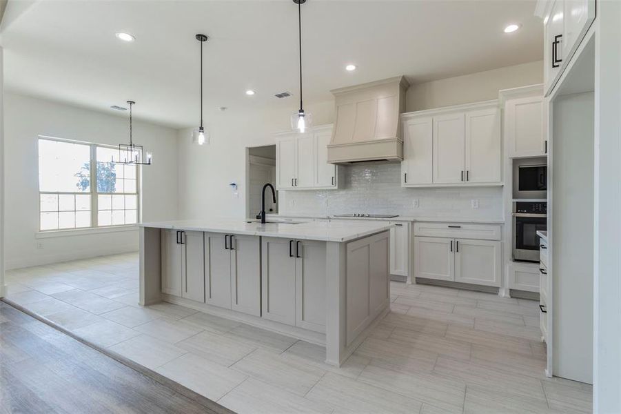 Kitchen featuring pendant lighting, sink, an island with sink, custom range hood, and stainless steel oven