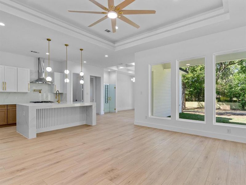 Kitchen with light hardwood / wood-style floors, decorative light fixtures, a raised ceiling, and wall chimney range hood