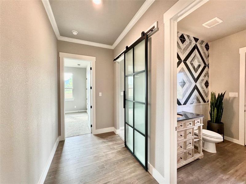 Corridor with a barn door, wood-type flooring, and crown molding