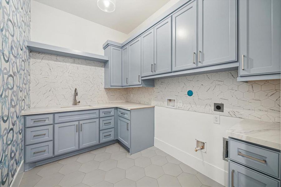 This large utility room is the epitome of style and functionality with quartz countertops, an undermount sink/pulldown faucet, geometric tiles, designer wallpaper and plenty of storage space.