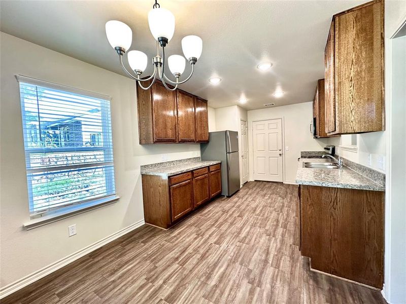 Kitchen with hardwood / wood-style flooring, stainless steel appliances, hanging light fixtures, and an inviting chandelier