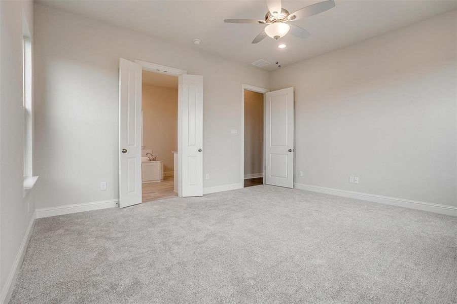 Unfurnished bedroom with connected bathroom, ceiling fan, and light colored carpet