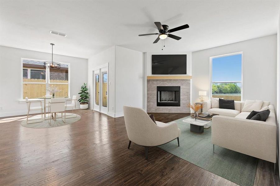 Living room featuring a healthy amount of sunlight, ceiling fan with notable chandelier, a tiled fireplace, and hardwood / wood-style flooring