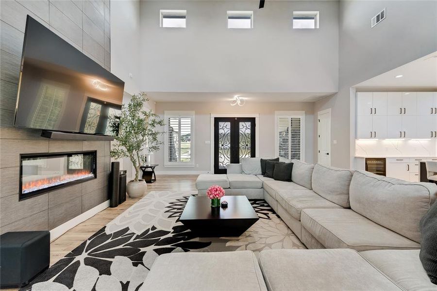 Living room featuring wine cooler, light wood-type flooring, french doors, a high ceiling, and a fireplace