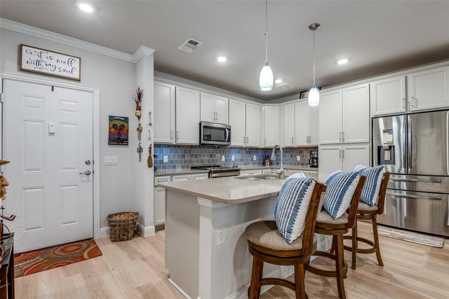 Kitchen with stainless steel appliances, crown molding, light wood-type flooring, and sink