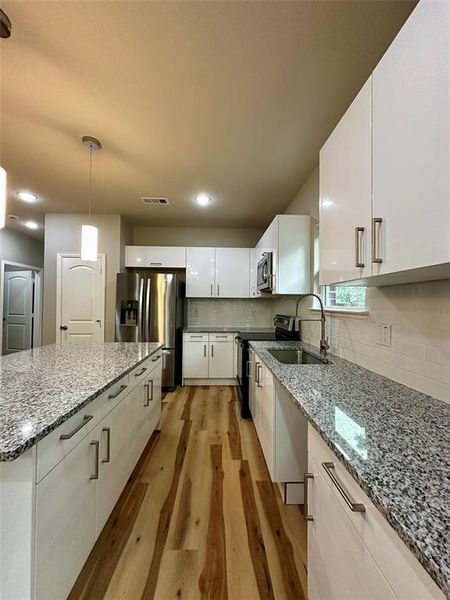 Kitchen featuring light wood-type flooring, backsplash, light stone countertops, decorative light fixtures, and sink