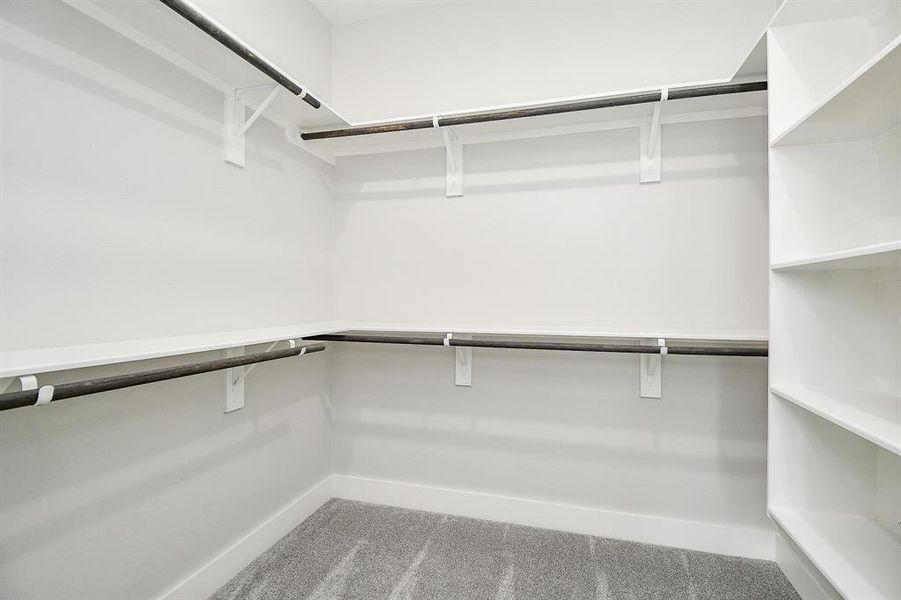 This is a spacious walk-in closet featuring ample shelving on one side and dual-level hanging rods on the other, all complemented by neutral carpeting and a clean, modern design.