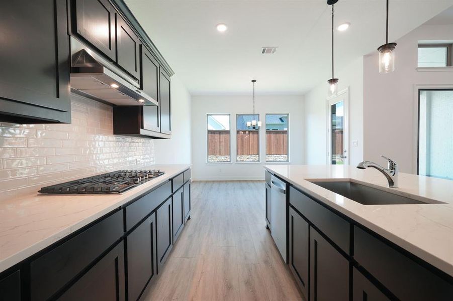 Kitchen featuring sink, hanging light fixtures, light hardwood / wood-style floors, and wall chimney range hood