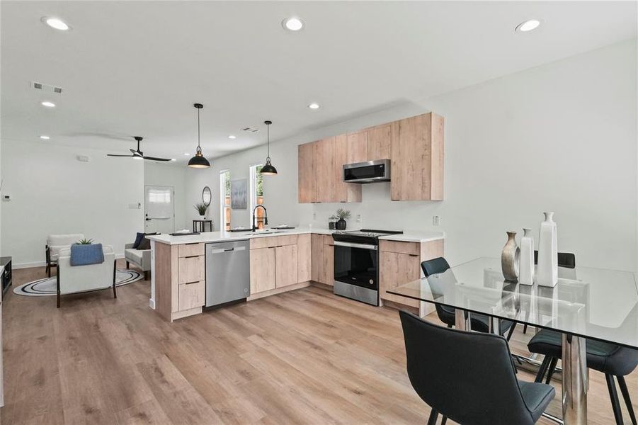 Kitchen with kitchen peninsula, decorative light fixtures, appliances with stainless steel finishes, light brown cabinetry, and light wood-type flooring