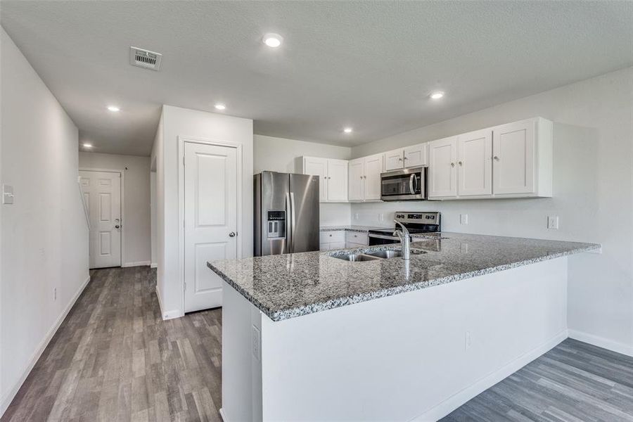 Kitchen featuring light wood-type flooring, white cabinets, kitchen peninsula, appliances with stainless steel finishes, and dark stone countertops