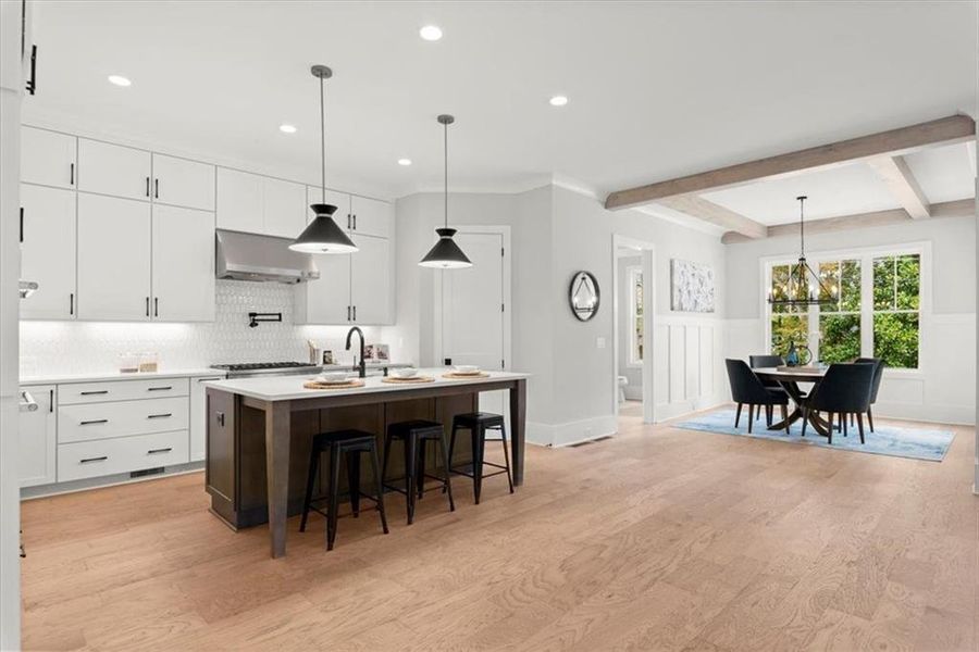 Kitchen with hanging light fixtures, light wood-type flooring, wall chimney exhaust hood, and white cabinetry