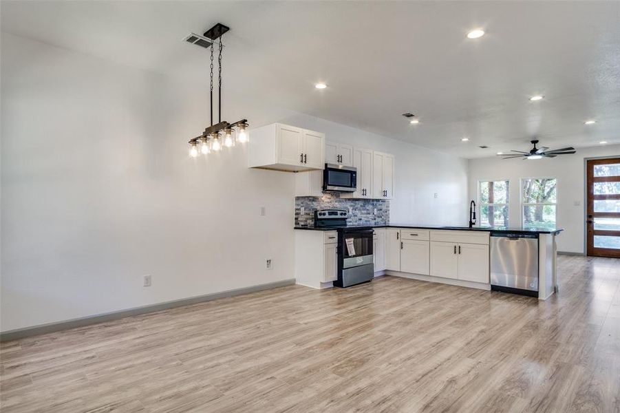 Kitchen featuring sink, decorative light fixtures, white cabinetry, appliances with stainless steel finishes, and light hardwood / wood-style floors