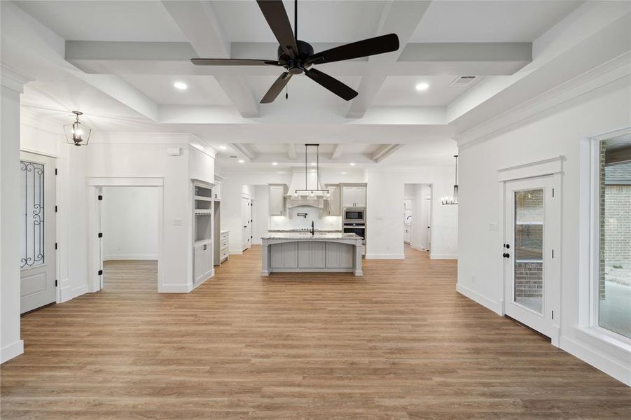 Kitchen featuring appliances with stainless steel finishes, light wood-type flooring, a center island with sink, and coffered ceiling