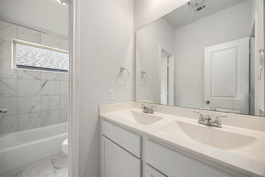 Secondary bathroom features light countertops and cabinets, neutral paint, shower/tub combo with tile surround, large mirror, tile floors, sleek fixtures and modern finishes, plenty of space to accommodate any visiting family or guests.